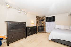 Bedroom with track lighting, a wood stove, and light carpet