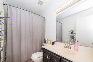 Full bath with curtained shower, visible vents, toilet, and vanity
