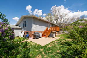 Rear view of house featuring a wooden deck, stairway, central AC unit, a patio area, and a yard