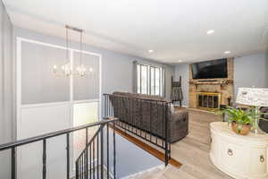 Living room featuring recessed lighting, light wood-style flooring, a stone fireplace, and a notable chandelier