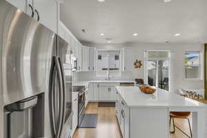 Kitchen featuring a kitchen breakfast bar, light wood-style floors, decorative backsplash, a kitchen island, and appliances with stainless steel finishes