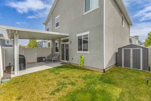 Rear view of house featuring fence, a shed, stucco siding, a patio, and a lawn