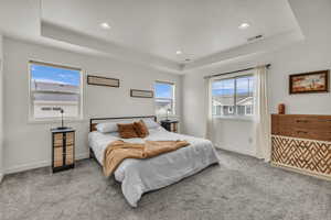 Bedroom featuring visible vents, a tray ceiling, and carpet flooring