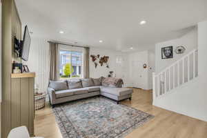 Living area featuring recessed lighting, light wood-style floors, a decorative wall, and stairs