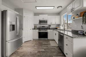 Kitchen featuring a sink, dark stone countertops, white cabinets, appliances with stainless steel finishes, and dark wood finished floors