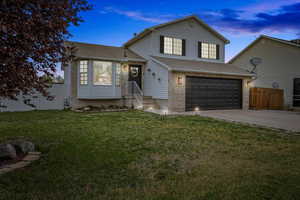 Split level home with a yard, fence, a shingled roof, a garage, and driveway