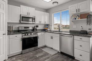 Kitchen with a sink, white cabinets, stainless steel appliances, and dark wood-type flooring