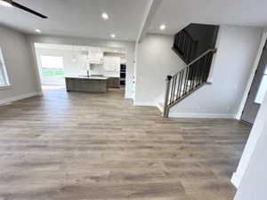 Unfurnished living room with baseboards, stairway, light wood-style flooring, and recessed lighting