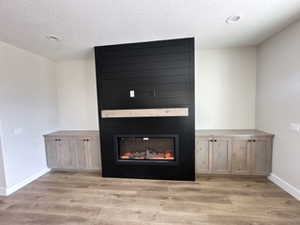 Unfurnished living room featuring a textured ceiling, baseboards, wood finished floors, and a glass covered fireplace