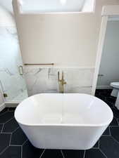 Full bathroom featuring a freestanding tub, a shower stall, wainscoting, and tile walls