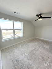 Bonus room with lofted ceiling, a textured ceiling, visible vents, ceiling fan, and baseboards