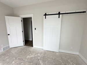 Unfurnished bedroom featuring visible vents, a barn door, and baseboards