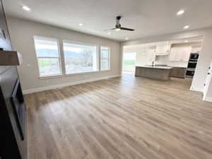 Unfurnished living room with baseboards, a ceiling fan, light wood-type flooring, and a large fireplace