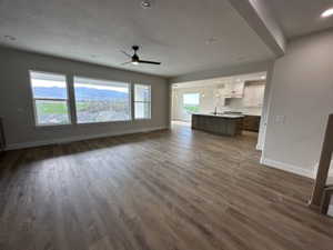 Unfurnished living room featuring baseboards, a ceiling fan, and dark wood-style flooring