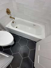 Bathroom with tile walls, tile patterned flooring, toilet, and a bathing tub