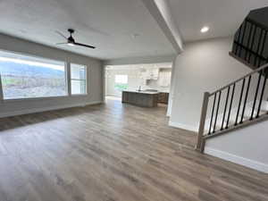 Unfurnished living room featuring recessed lighting, a ceiling fan, stairs, baseboards, and wood finished floors