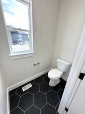 Bathroom with toilet, visible vents, and baseboards