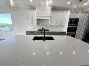 Kitchen featuring white cabinetry, a sink, stovetop, light stone countertops, and stainless steel oven