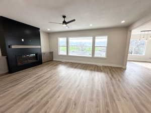 Unfurnished living room featuring recessed lighting, a glass covered fireplace, a ceiling fan, baseboards, and wood finished floors