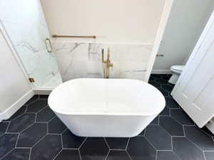 Full bathroom featuring toilet, a soaking tub, a stall shower, and wainscoting
