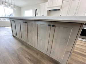 Kitchen with light countertops, pendant lighting, white cabinets, and light wood-type flooring