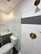 Full bath with toilet, a tile shower, visible vents, and vanity