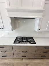 Details with white cabinets, light stone countertops, stainless steel gas stovetop, and premium range hood