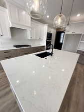 Kitchen featuring an island with sink, white cabinets, black stovetop, a sink, and dark wood-type flooring