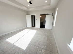 Unfurnished bedroom featuring a barn door, a ceiling fan, a tray ceiling, and baseboards