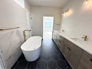 Bathroom featuring double vanity, a sink, a freestanding tub, and tile walls