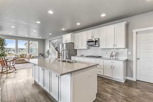 Kitchen featuring a sink, dark wood-type flooring, a center island with sink, appliances with stainless steel finishes, and white cabinetry