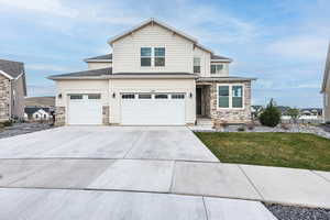 View of front facade with a front lawn, driveway, stone siding, and a garage
