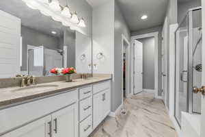 Full bathroom featuring marble finish floor, a sink, double vanity, and a stall shower