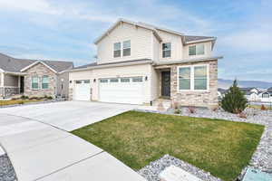 View of front facade featuring stone siding, an attached garage, driveway, and a front yard