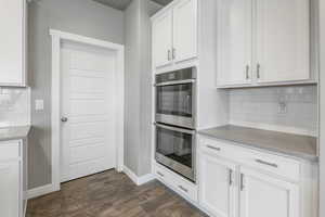 Kitchen with backsplash, baseboards, dark wood finished floors, and double oven