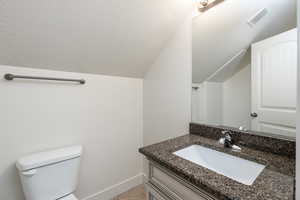 Half bathroom featuring vanity, toilet, visible vents, vaulted ceiling, and baseboards