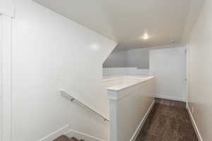 Hallway with baseboards, dark carpet, and an upstairs landing