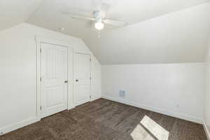 Additional living space with dark colored carpet, ceiling fan, baseboards, visible vents, and lofted ceiling