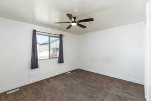 Spare room with baseboards, visible vents, dark colored carpet, and a ceiling fan
