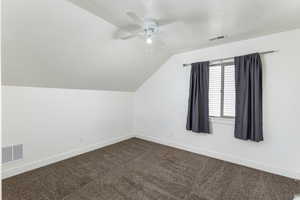 Additional living space with a ceiling fan, visible vents, dark carpet, and vaulted ceiling