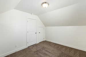 Additional living space with vaulted ceiling, dark colored carpet, and baseboards