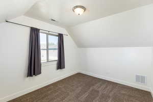Additional living space with visible vents, dark carpet, lofted ceiling, and baseboards