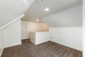 Additional living space with lofted ceiling, visible vents, dark colored carpet, and baseboards