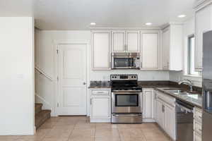 Kitchen featuring dark stone countertops, recessed lighting, light tile patterned floors, appliances with stainless steel finishes, and a sink