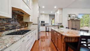 Kitchen featuring stainless steel appliances, a kitchen breakfast bar, wood finished floors, recessed lighting, and light stone countertops