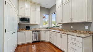 Kitchen with appliances with stainless steel finishes, dark wood-type flooring, light stone counters, and white cabinets
