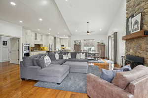 Living area with a stone fireplace, wood finished floors, ceiling fan, high vaulted ceiling, and recessed lighting