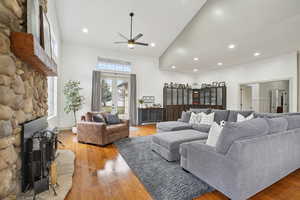 Living room featuring high vaulted ceiling, a ceiling fan, light wood finished floors, recessed lighting, and a stone fireplace