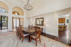 Dining area with a towering ceiling, a notable chandelier, wood finished floors, and baseboards