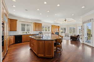 Kitchen featuring an island with sink, backsplash, crown molding, dark stone counters, and black dishwasher